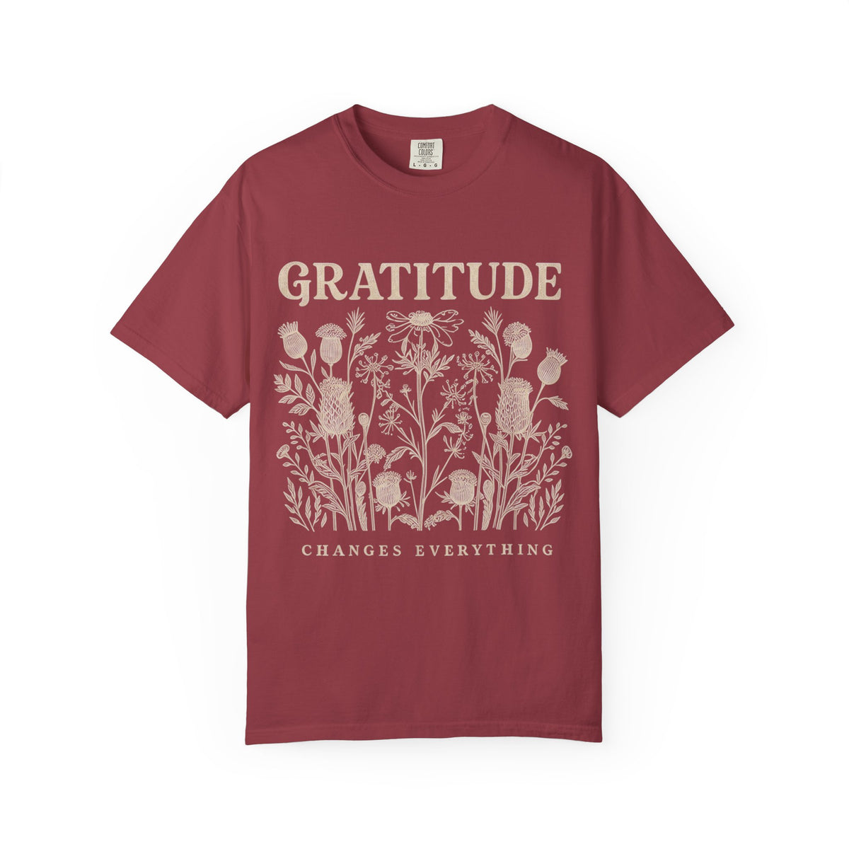 A maroon short-sleeve crewneck t-shirt with a cream-colored graphic print featuring the word 'GRATITUDE' above a cluster of wildflowers and the phrase 'CHANGES EVERYTHING' below, displayed on a clean white background.