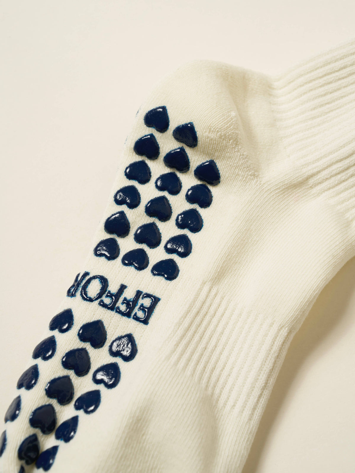 Close-up of navy heart-shaped non-slip grips on the cushioned ivory sock sole