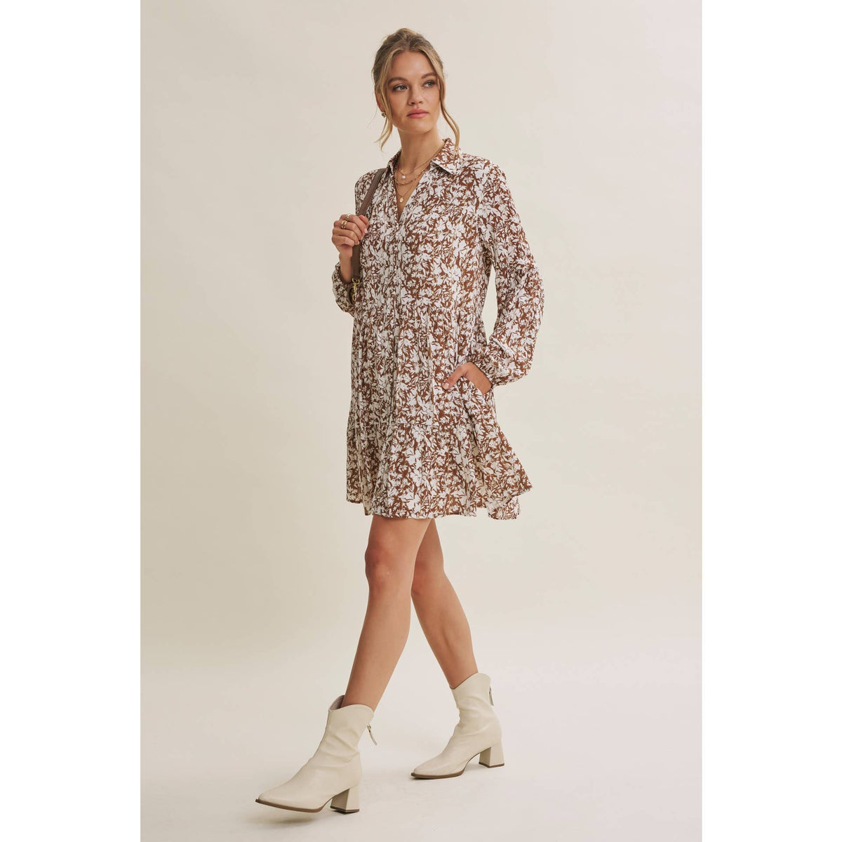 Three-quarter view of the mocha and cream floral mini dress with a shoulder bag and cream boots.