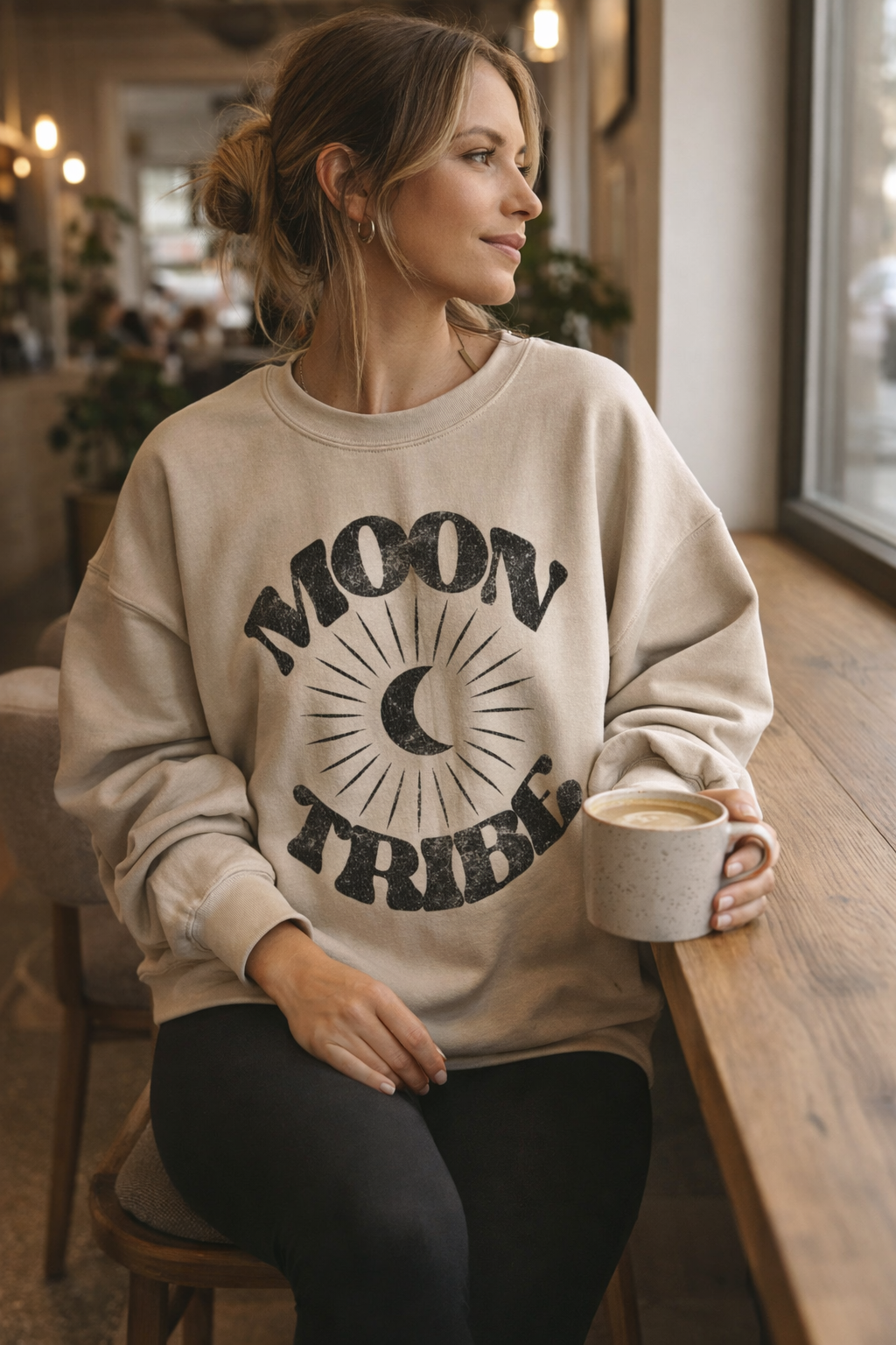 Woman wearing Lunar Essence Moon Tribe sweatshirt with denim in a coffee shop