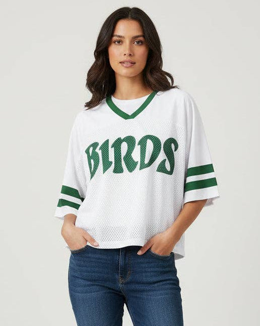 Woman modeling the white cropped mesh B1RDS jersey with Kelly green V-neck and sleeve stripes.