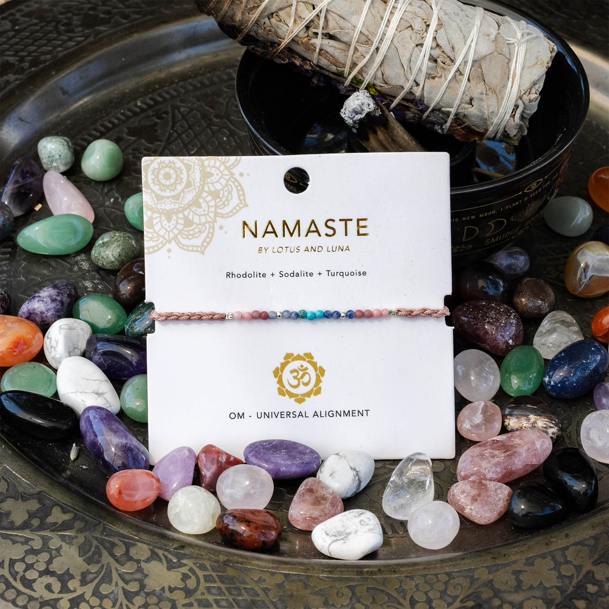 Packaged Om Namaste bracelet styled among colorful natural stones and cleansing sage
