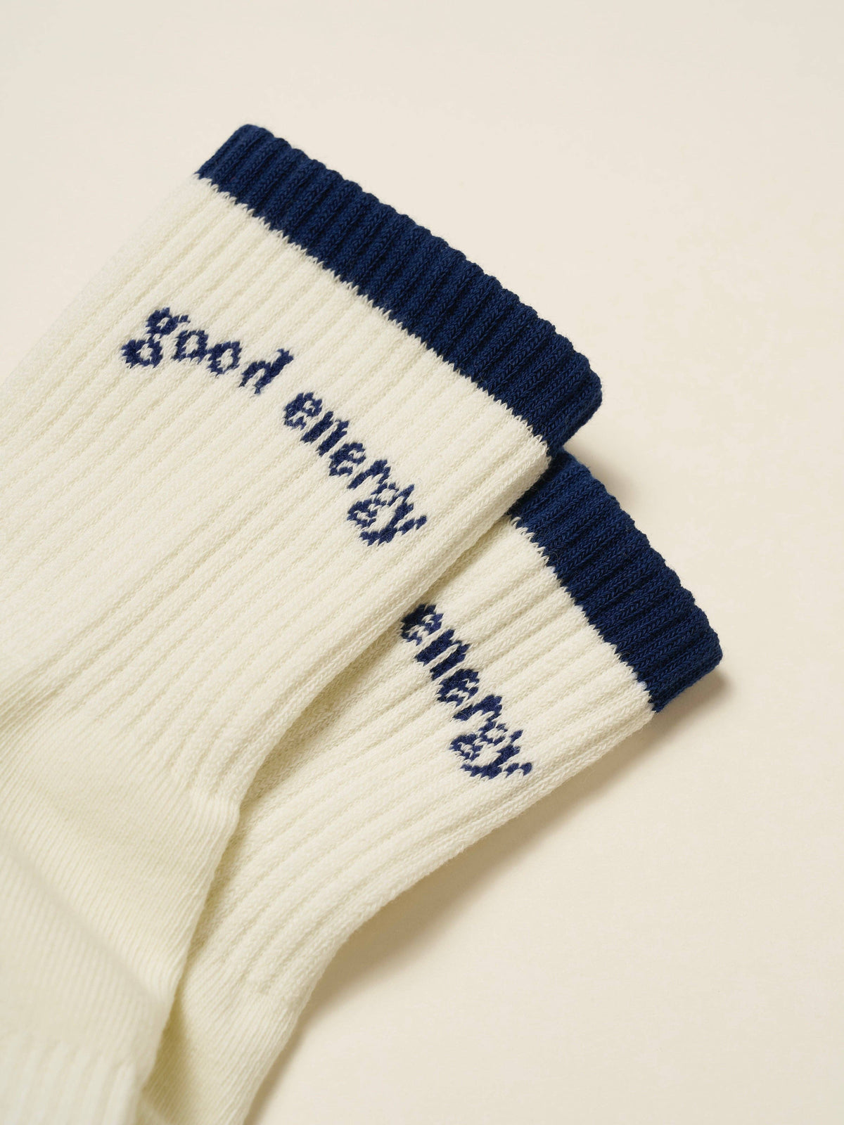 Close-up of ivory ribbed socks with navy cuffs and Good Energy embroidery