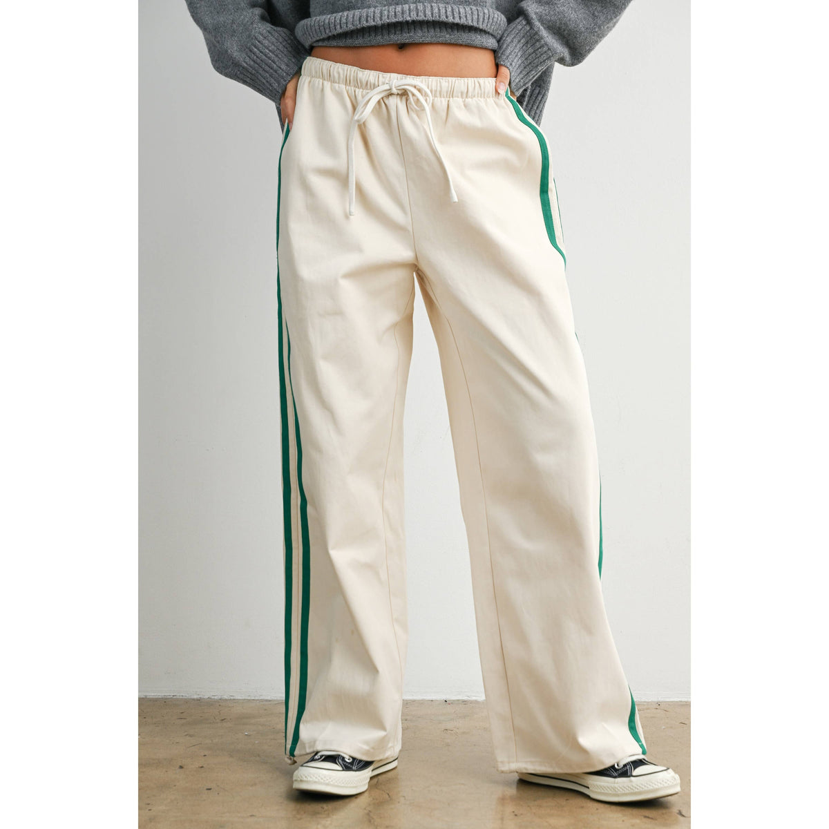 Ivory wide-leg drawstring track pants with green side stripes, front three-quarter view