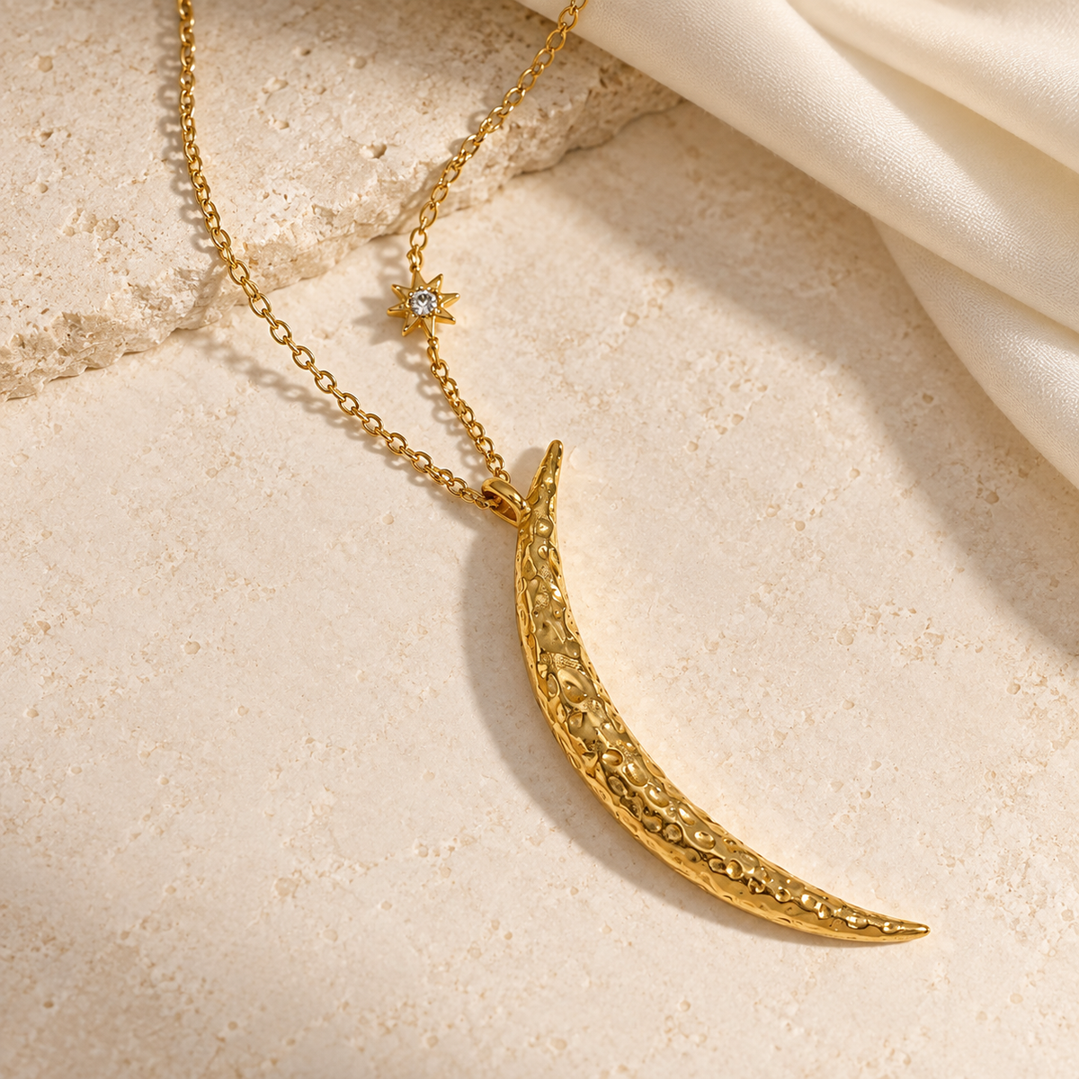 Luna & Light gold crescent moon necklace with a textured pendant and starburst accent, styled on warm ivory stone.