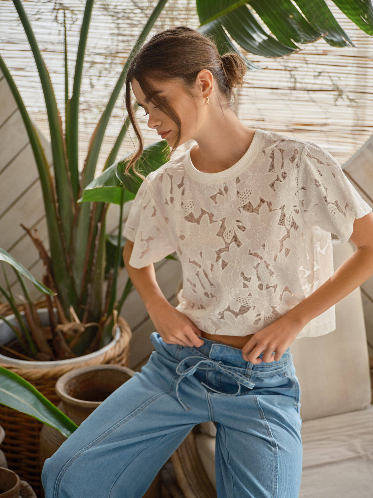 Off-white Soft Bloom Floral Lace Tee with a crew neckline and short sleeves, styled with blue jeans beside indoor plants
