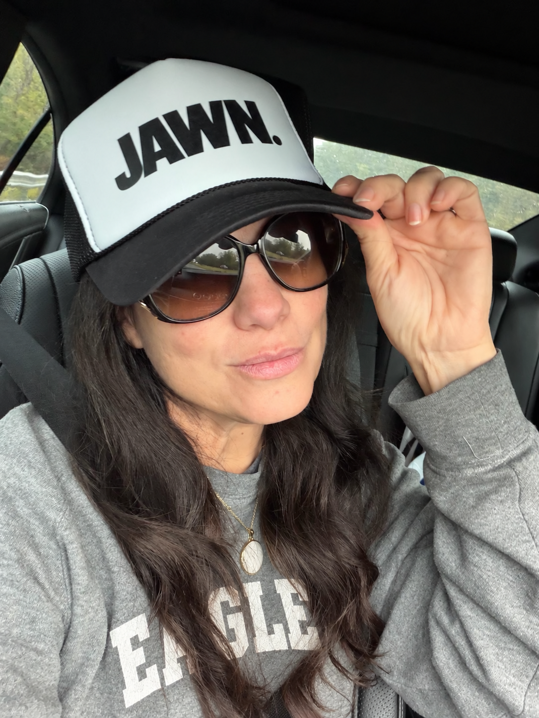 Woman wearing the black-and-white JAWN. trucker hat with a gray Eagles sweatshirt, showing the hat's structured front and curved brim.