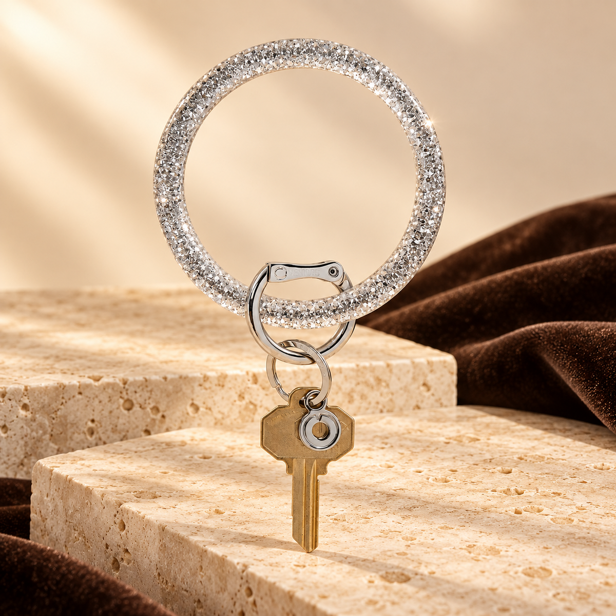 Resin Big O Disco Ball Sparkle bracelet keychain with silver hardware and a brass key on cream stone