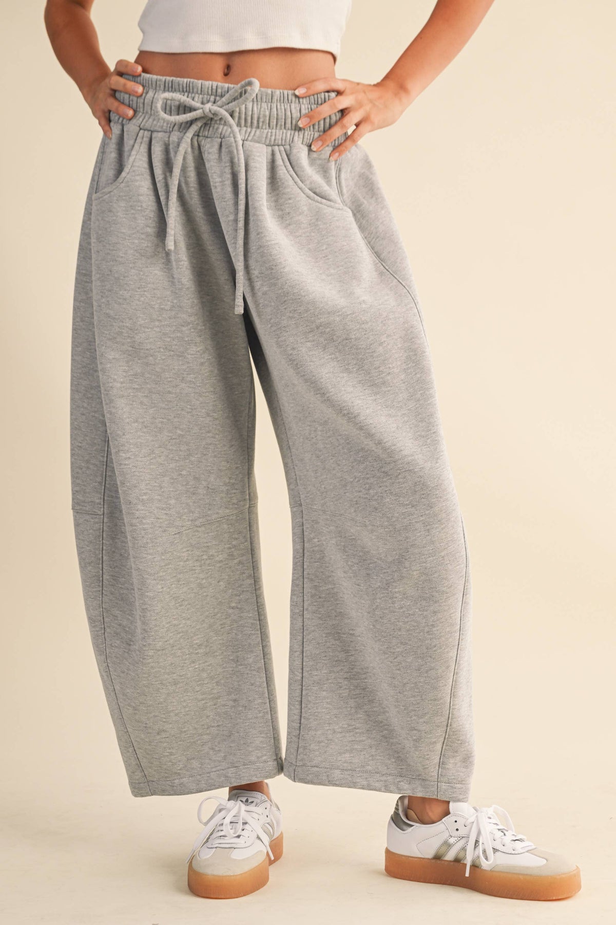 A person wearing light heather gray wide-leg sweatpants with an elastic drawstring waist, paired with white sneakers, against a plain beige studio background.