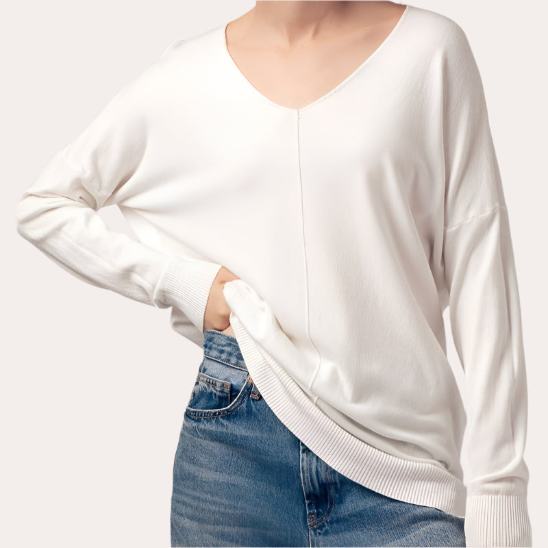 A woman wearing a beige high-low tunic sweater with a V-neckline and long sleeves, paired with blue jeans.