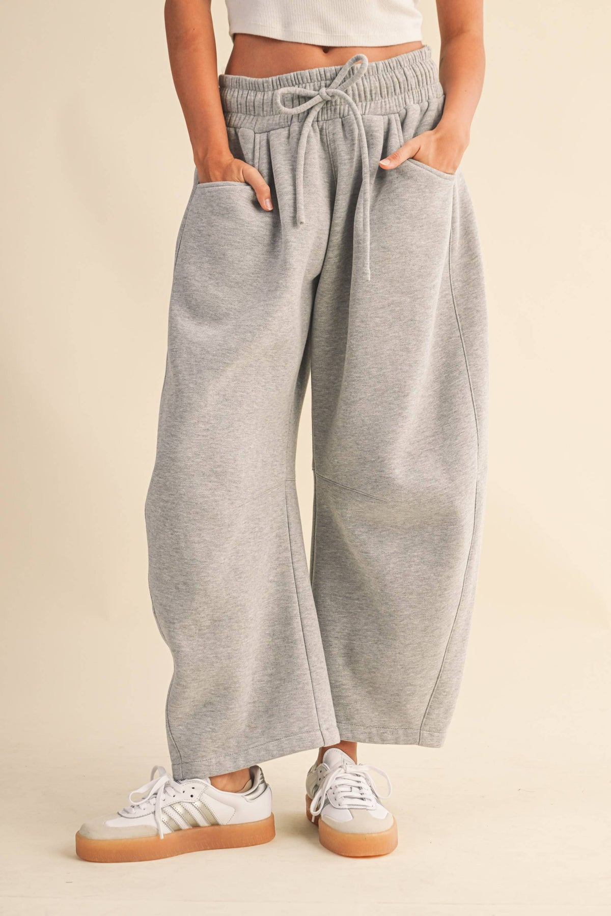 A person wearing light heather gray wide-leg sweatpants with an elastic drawstring waist and side pockets, paired with white sneakers, against a plain beige studio background.