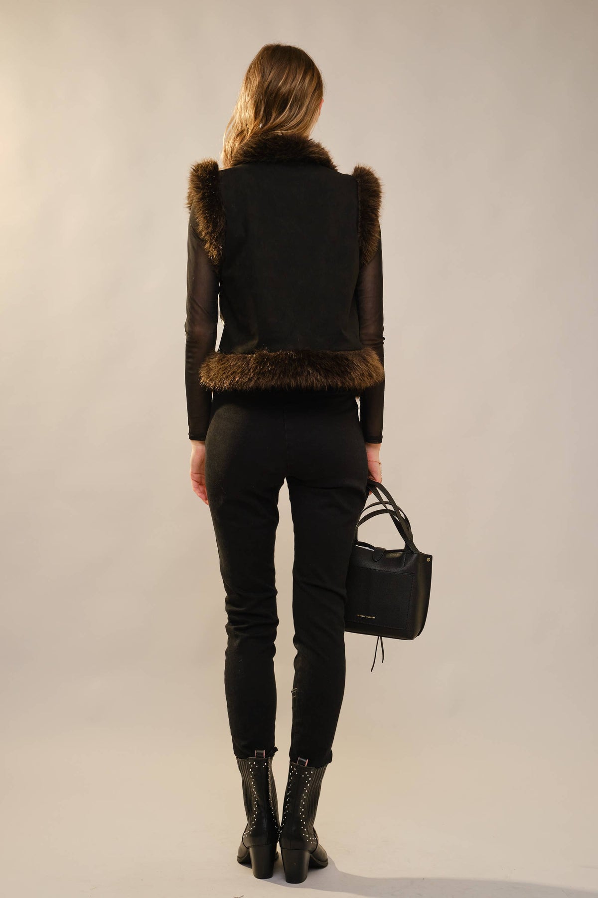 Person wearing a black outfit with fur details on a plain background