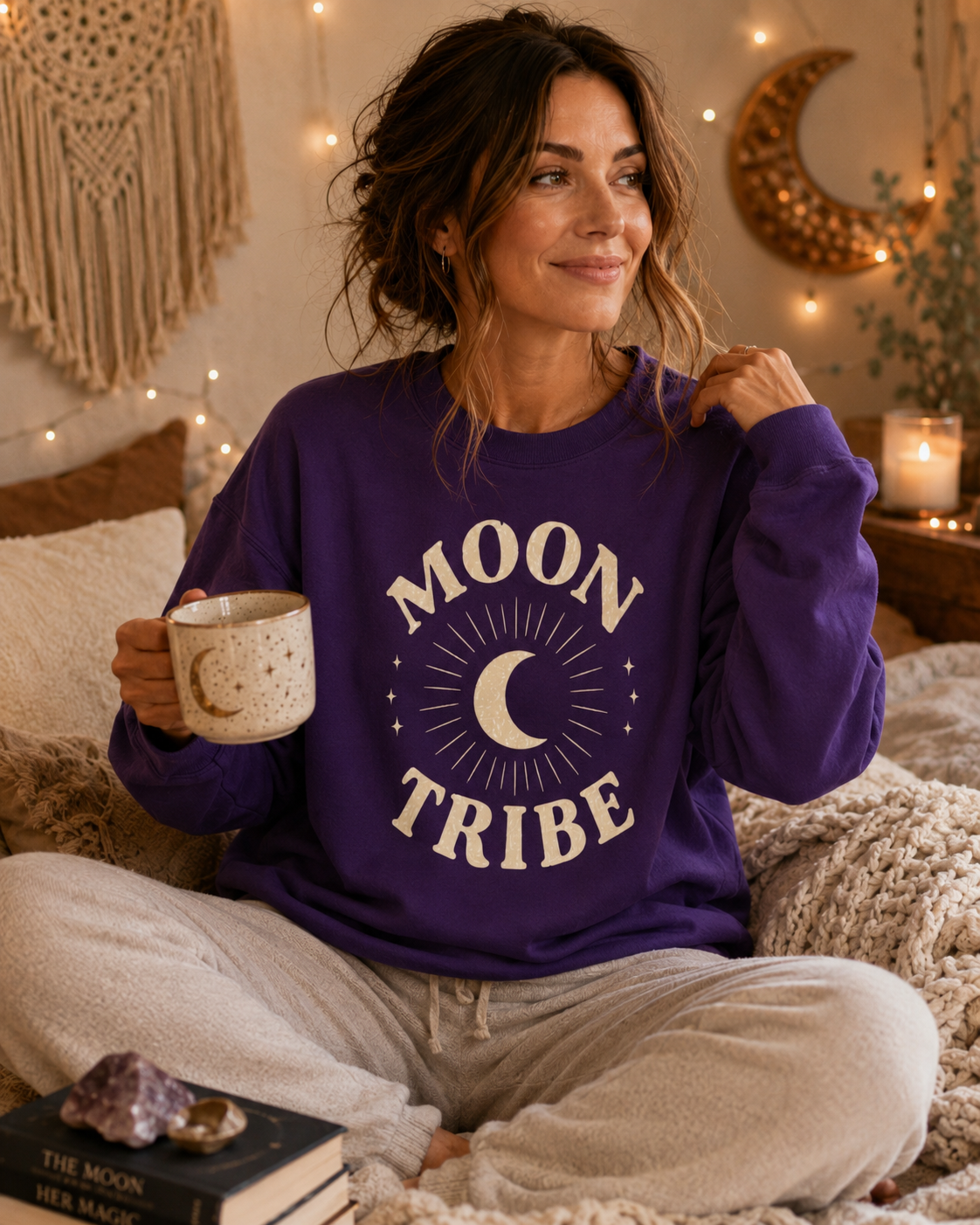Woman wearing a purple 'Moon Tribe' sweatshirt in a cozy room.