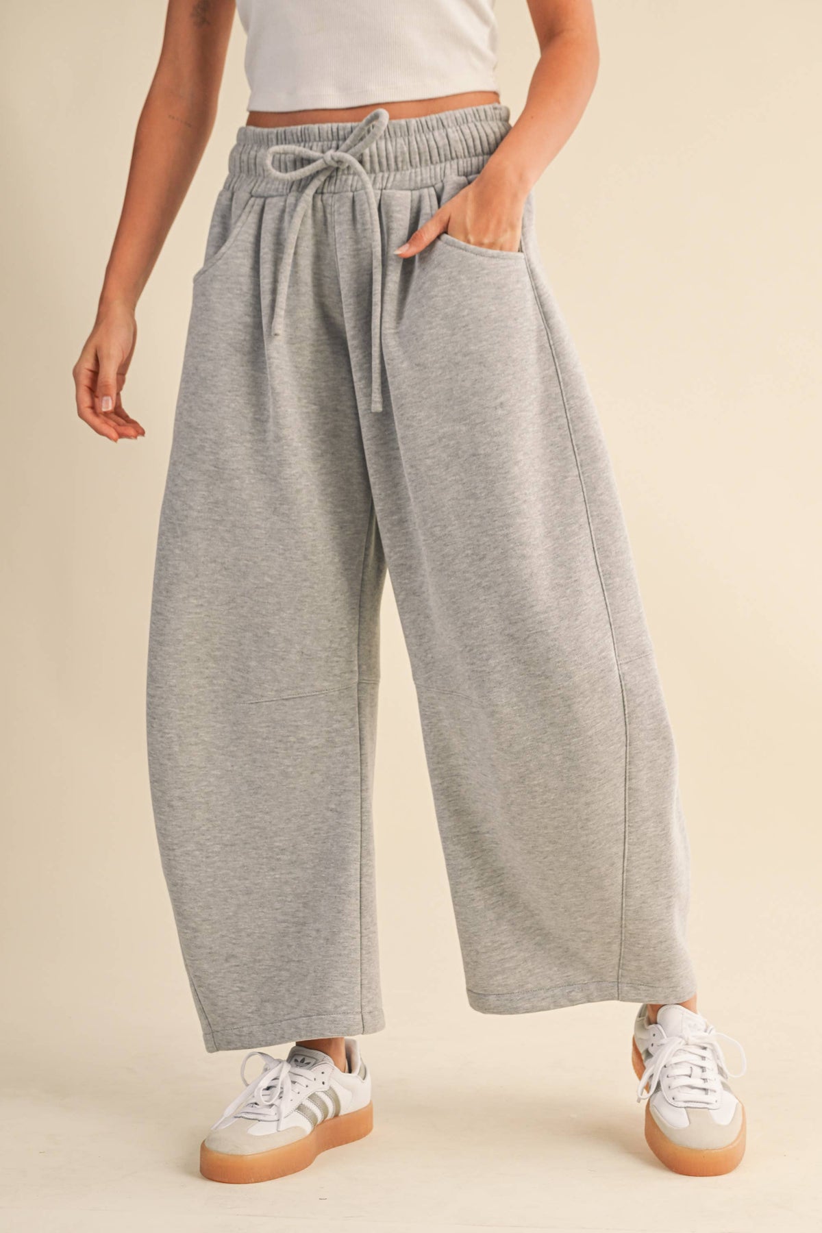 A person wearing light heather gray wide-leg sweatpants with an elastic drawstring waist, paired with white sneakers, against a plain beige studio background.