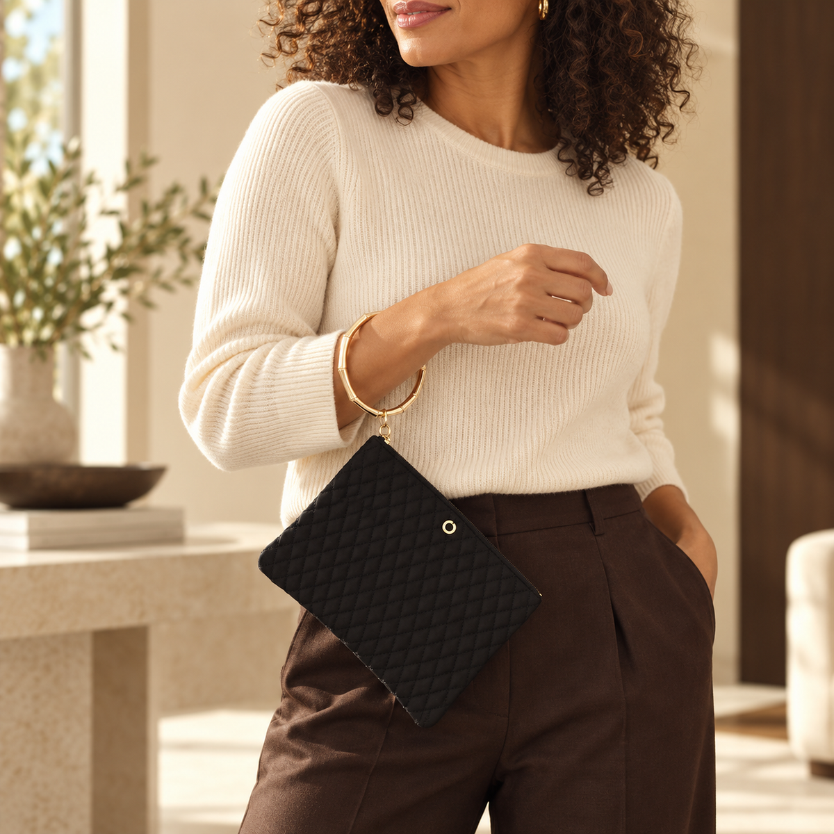 Woman wearing the black quilted Big O bracelet pouch hands-free with cream knit and chocolate trousers