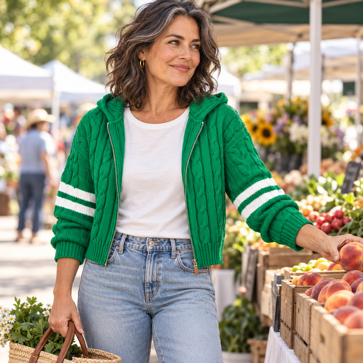 House of Caelo green cable-knit hooded cardigan with ivory sleeve stripes on a mature woman shopping at a farmers market